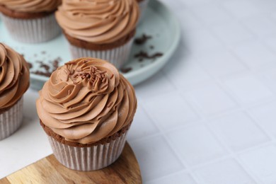 Photo of Tasty cupcakes with chocolate cream on white tiled table, closeup. Space for text