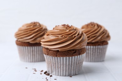 Photo of Tasty cupcakes with chocolate cream on white tiled table, closeup