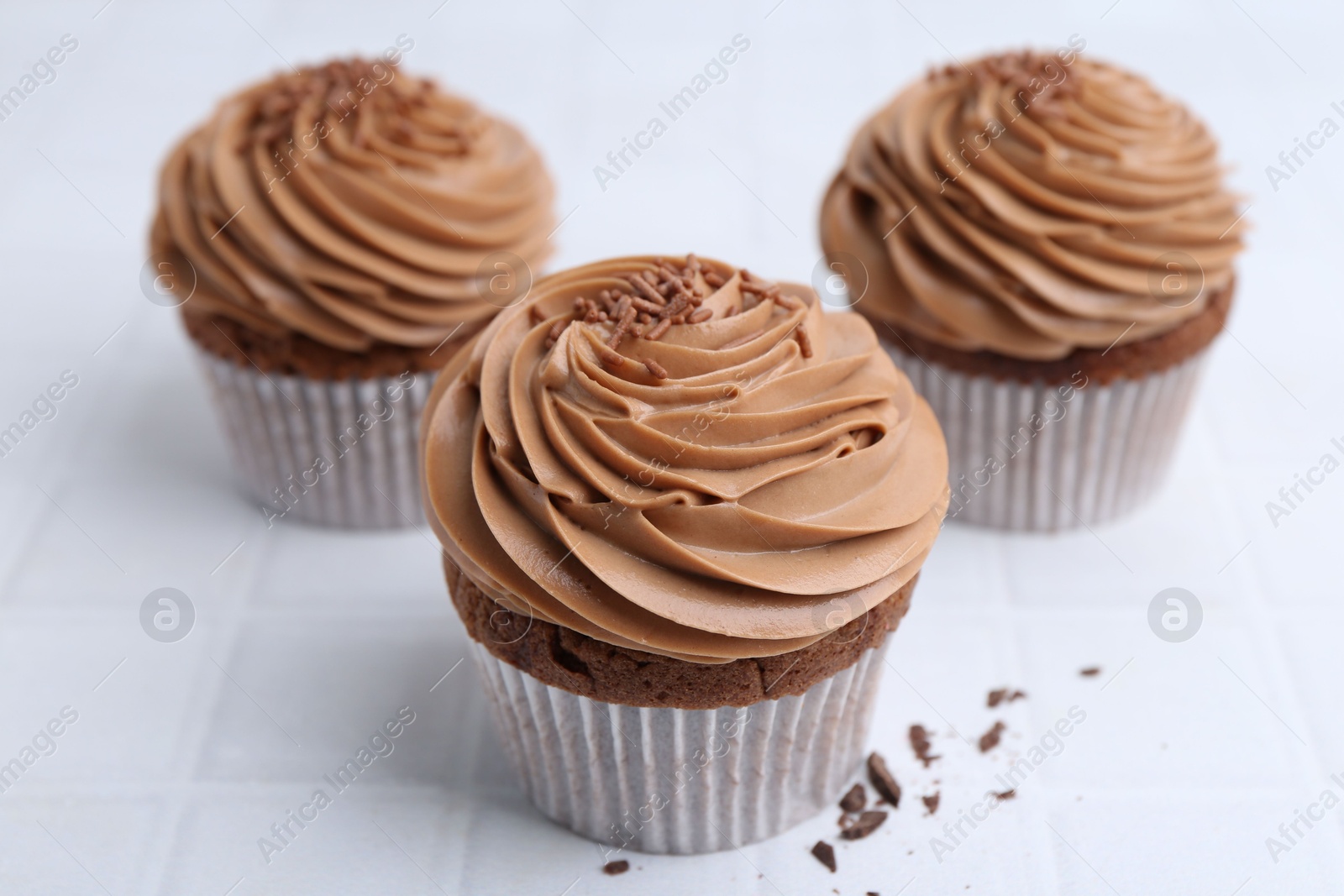 Photo of Tasty cupcakes with chocolate cream on white tiled table, closeup