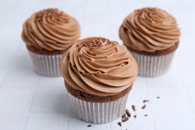 Photo of Tasty cupcakes with chocolate cream on white tiled table, closeup