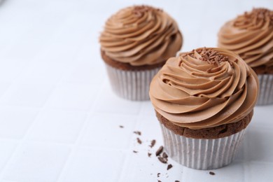 Photo of Tasty cupcakes with chocolate cream on white tiled table, closeup. Space for text