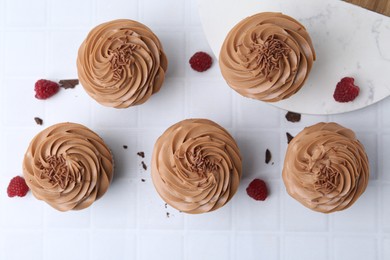 Photo of Tasty cupcakes with chocolate cream and raspberries on white tiled table, flat lay