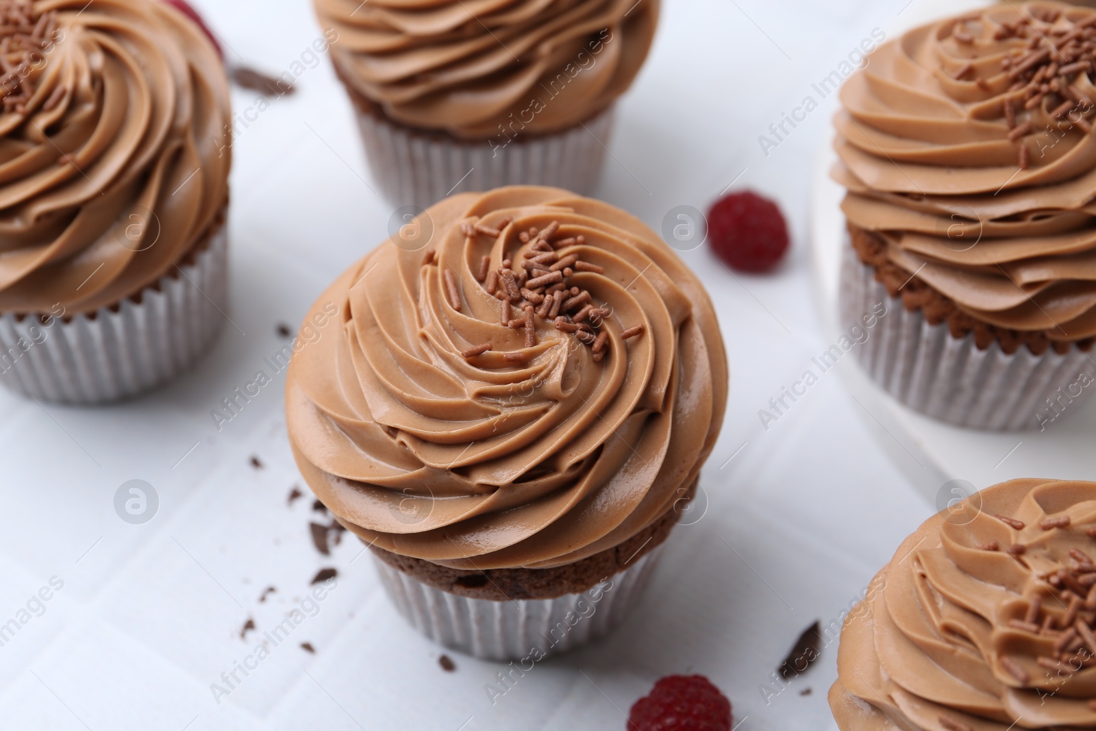 Photo of Tasty cupcakes with chocolate cream and raspberries on white tiled table, closeup