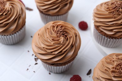 Photo of Tasty cupcakes with chocolate cream and raspberries on white tiled table, closeup