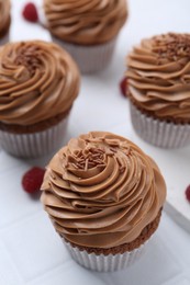 Photo of Tasty cupcakes with chocolate cream and raspberries on white tiled table, closeup