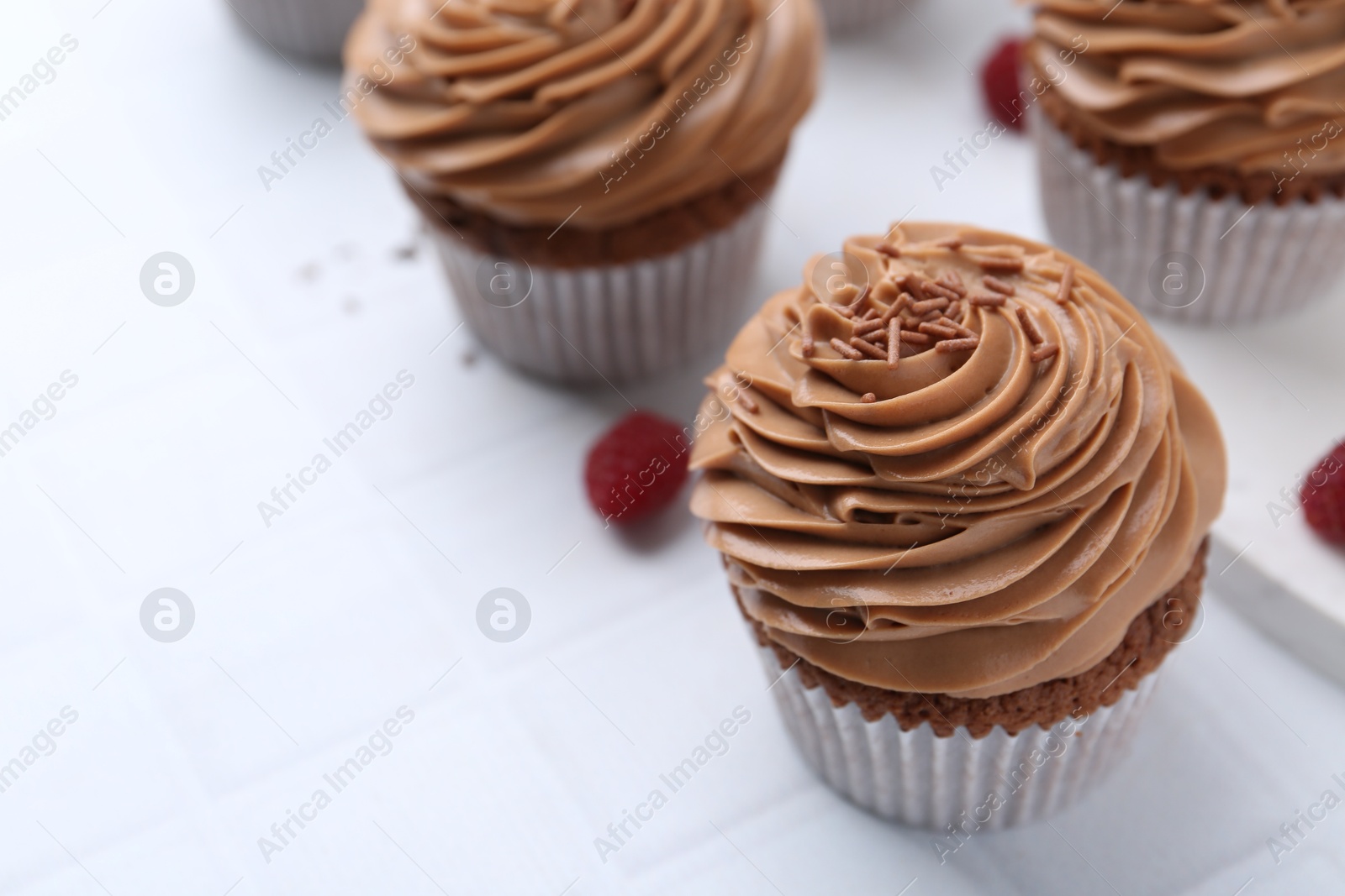 Photo of Tasty cupcakes with chocolate cream and raspberries on white tiled table, closeup. Space for text