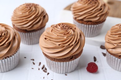 Photo of Tasty cupcakes with chocolate cream on white tiled table, closeup