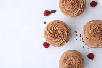 Photo of Tasty cupcakes with chocolate cream and raspberries on white tiled table, flat lay. Space for text