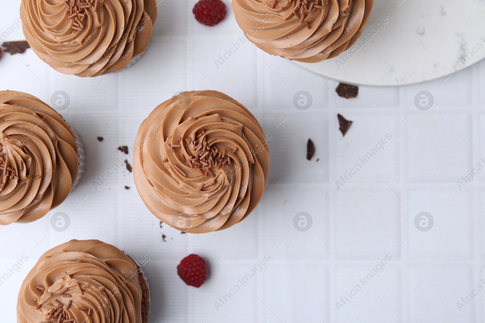 Photo of Tasty cupcakes with chocolate cream and raspberries on white tiled table, flat lay. Space for text