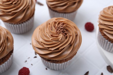 Photo of Tasty cupcakes with chocolate cream and raspberries on white tiled table, closeup