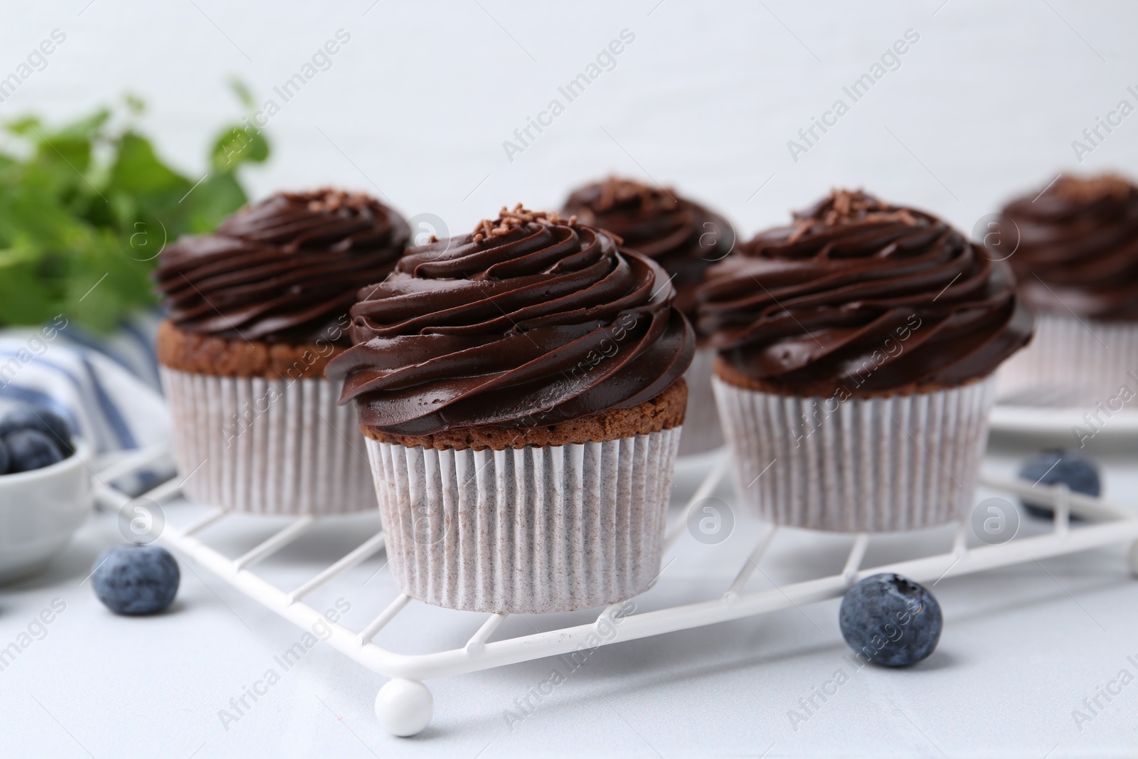 Photo of Tasty cupcakes with chocolate cream and blueberries on white tiled table, closeup