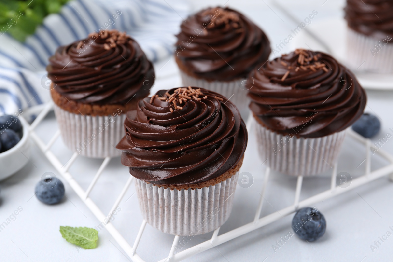 Photo of Tasty cupcakes with chocolate cream and blueberries on white tiled table, closeup