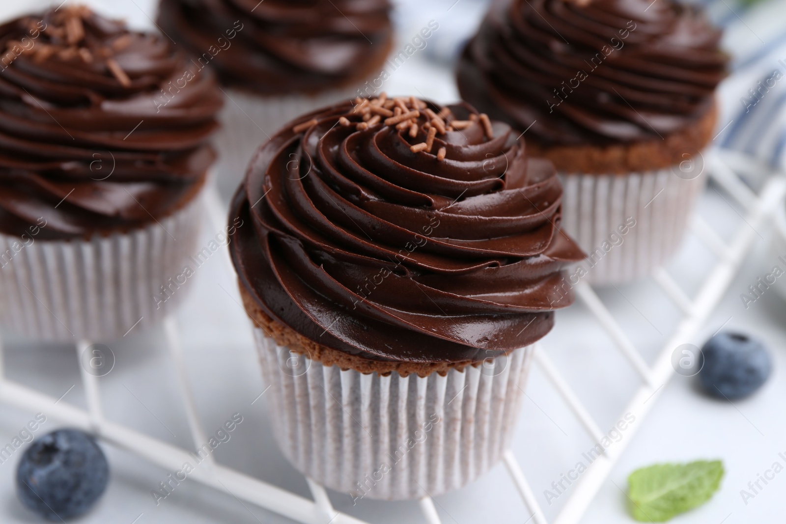 Photo of Tasty cupcakes with chocolate cream and blueberries on white tiled table, closeup