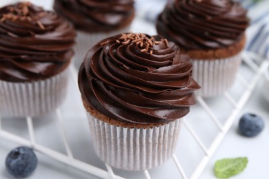 Photo of Tasty cupcakes with chocolate cream and blueberries on white tiled table, closeup