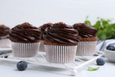 Photo of Tasty cupcakes with chocolate cream and blueberries on white tiled table, closeup