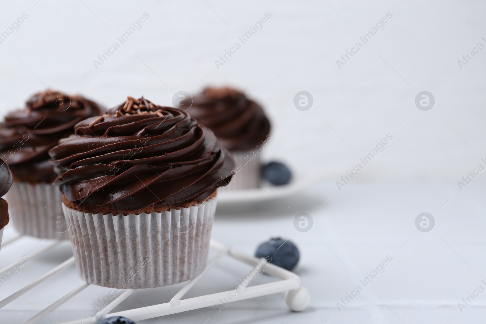 Photo of Tasty cupcakes with chocolate cream and blueberries on white tiled table, closeup. Space for text