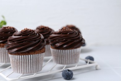 Photo of Tasty cupcakes with chocolate cream and blueberries on white tiled table, closeup