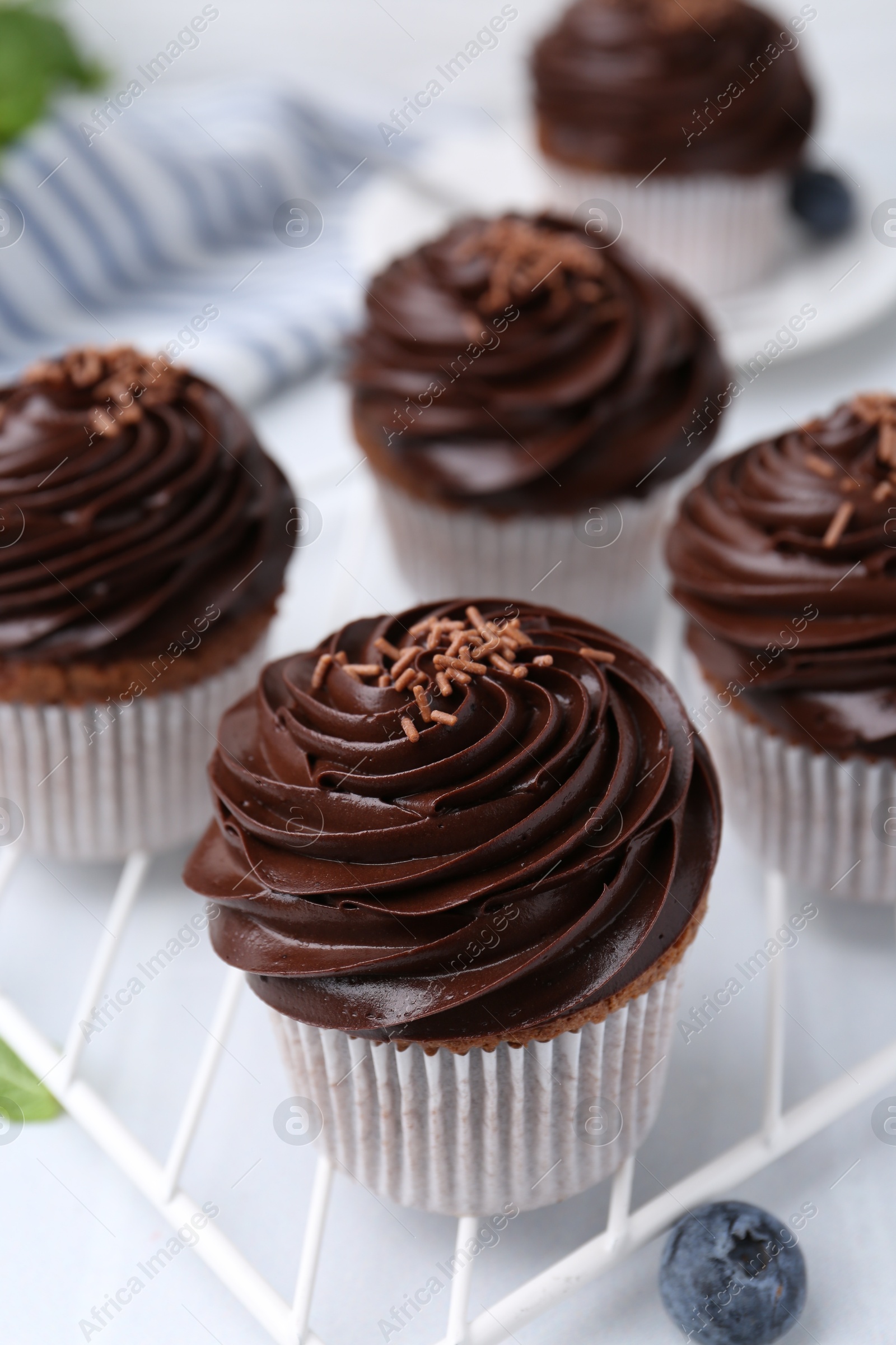 Photo of Tasty cupcakes with chocolate cream and blueberries on white tiled table, closeup