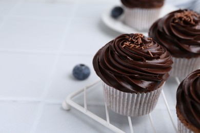 Photo of Tasty cupcakes with chocolate cream and blueberries on white tiled table, closeup. Space for text