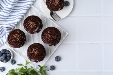 Photo of Tasty cupcakes with chocolate cream and blueberries on white tiled table, flat lay. Space for text