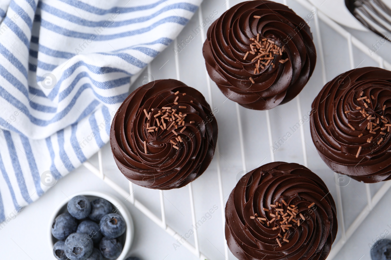 Photo of Tasty cupcakes with chocolate cream and blueberries on white tiled table, flat lay