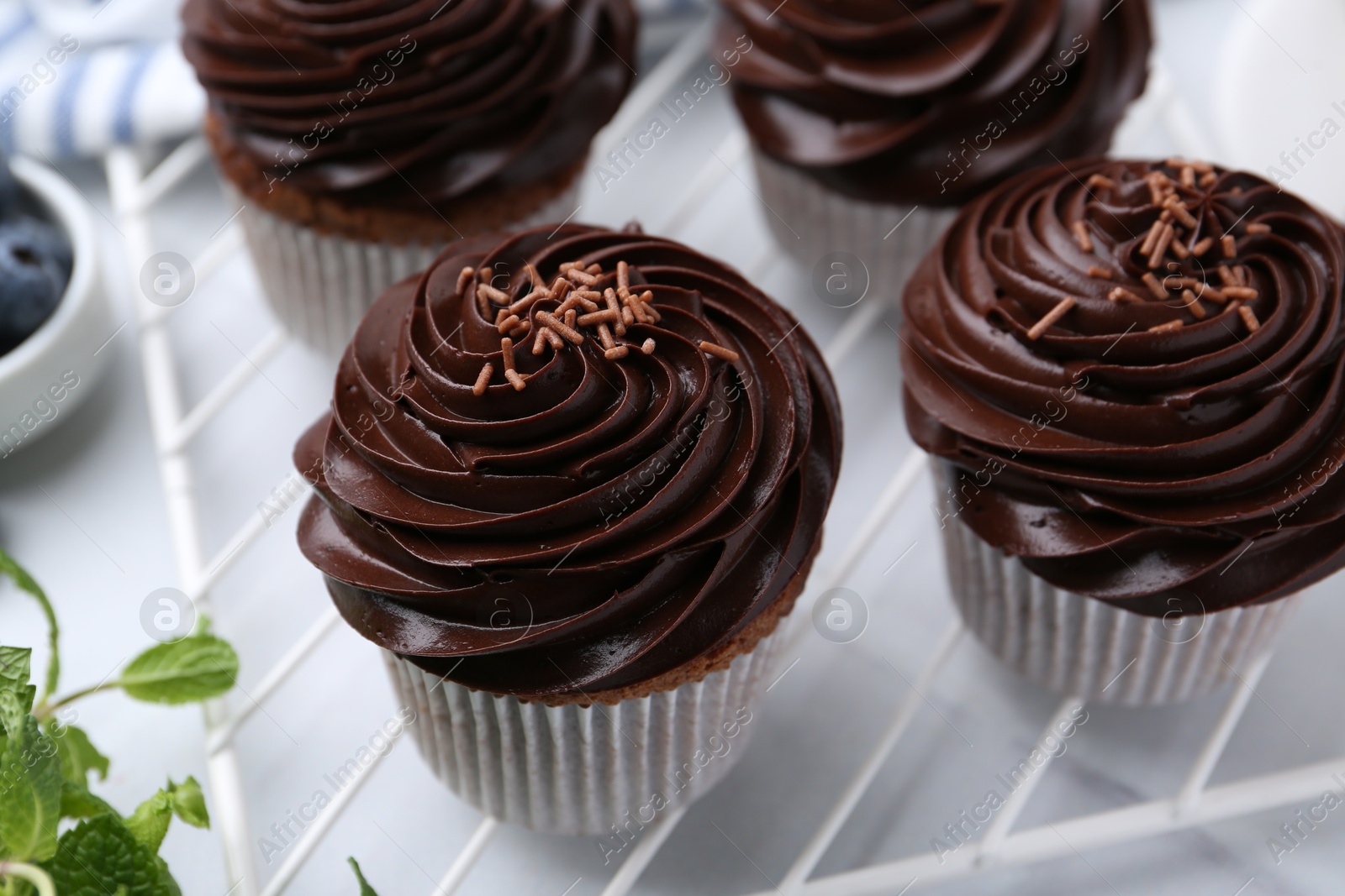 Photo of Tasty cupcakes with chocolate cream on white tiled table, closeup