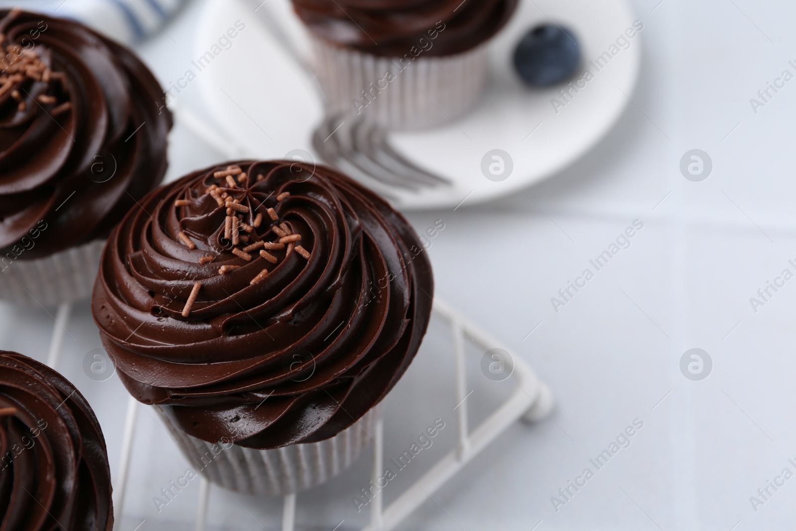 Photo of Tasty cupcakes with chocolate cream on white tiled table, closeup. Space for text