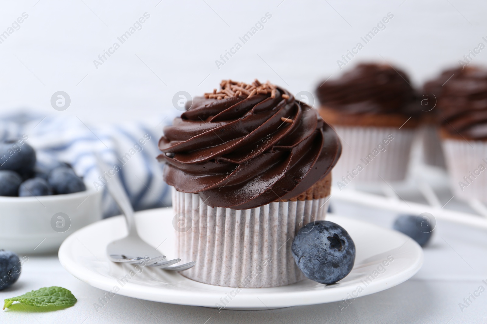 Photo of Tasty cupcakes with chocolate cream and blueberries on white tiled table, closeup