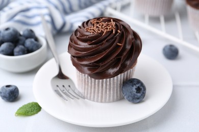 Photo of Tasty cupcake with chocolate cream and blueberries on white tiled table, closeup