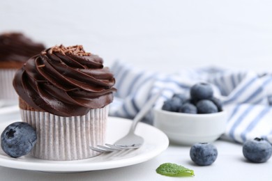 Photo of Tasty cupcake with chocolate cream and blueberries on white tiled table, closeup