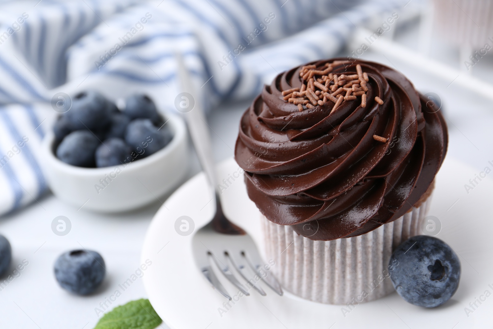 Photo of Tasty cupcake with chocolate cream and blueberries on white tiled table, closeup