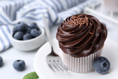 Photo of Tasty cupcake with chocolate cream and blueberries on white tiled table, closeup