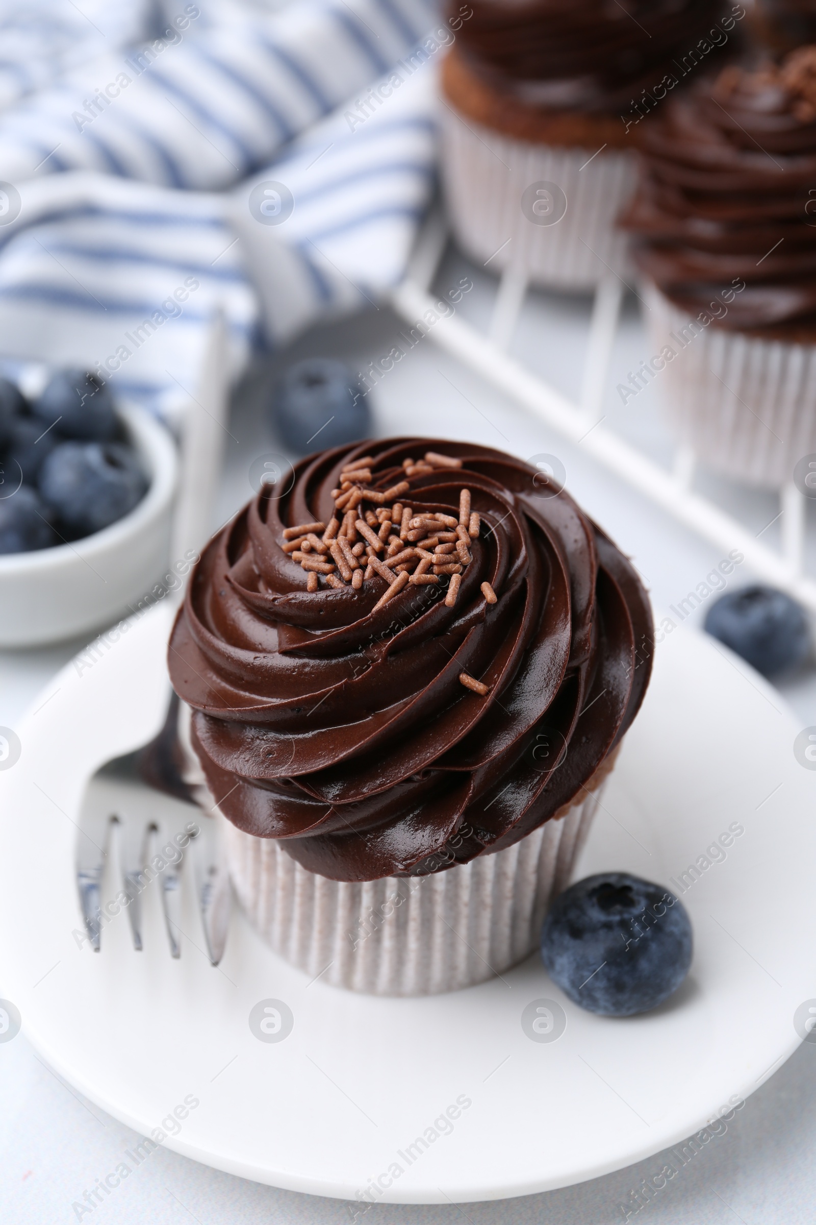 Photo of Tasty cupcakes with chocolate cream and blueberries on white tiled table, closeup