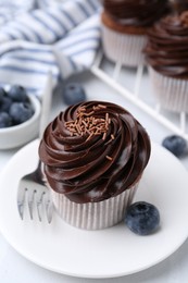 Photo of Tasty cupcakes with chocolate cream and blueberries on white tiled table, closeup