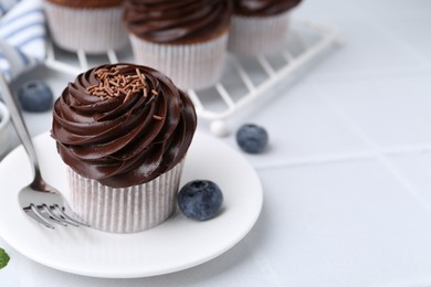 Photo of Tasty cupcakes with chocolate cream and blueberries on white tiled table, closeup. Space for text