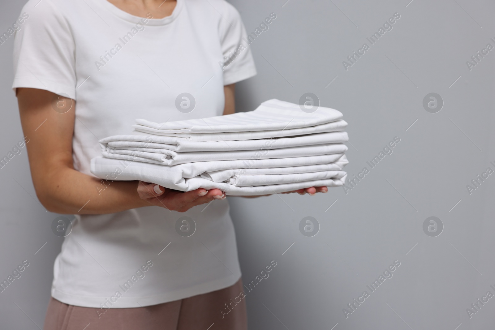 Photo of Woman with clean bed linens on grey background, closeup