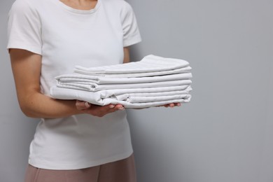 Woman with clean bed linens on grey background, closeup