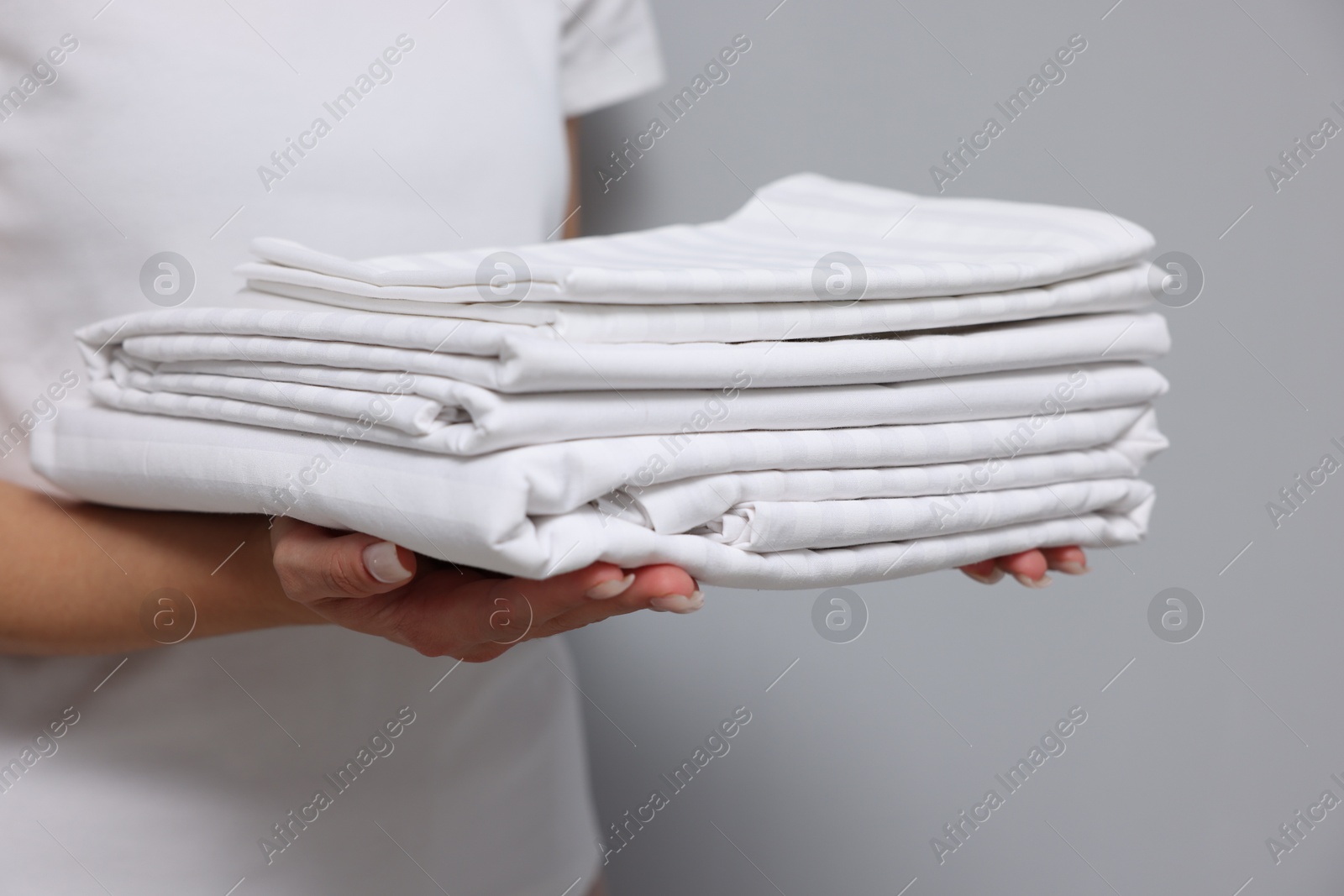 Photo of Woman with clean bed linens on grey background, closeup