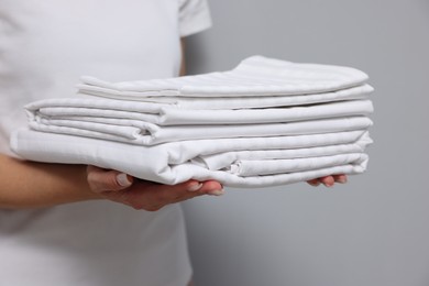 Woman with clean bed linens on grey background, closeup