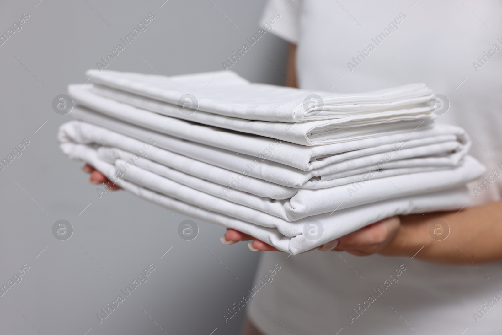 Photo of Woman with clean bed linens on grey background, closeup