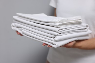 Woman with clean bed linens on grey background, closeup