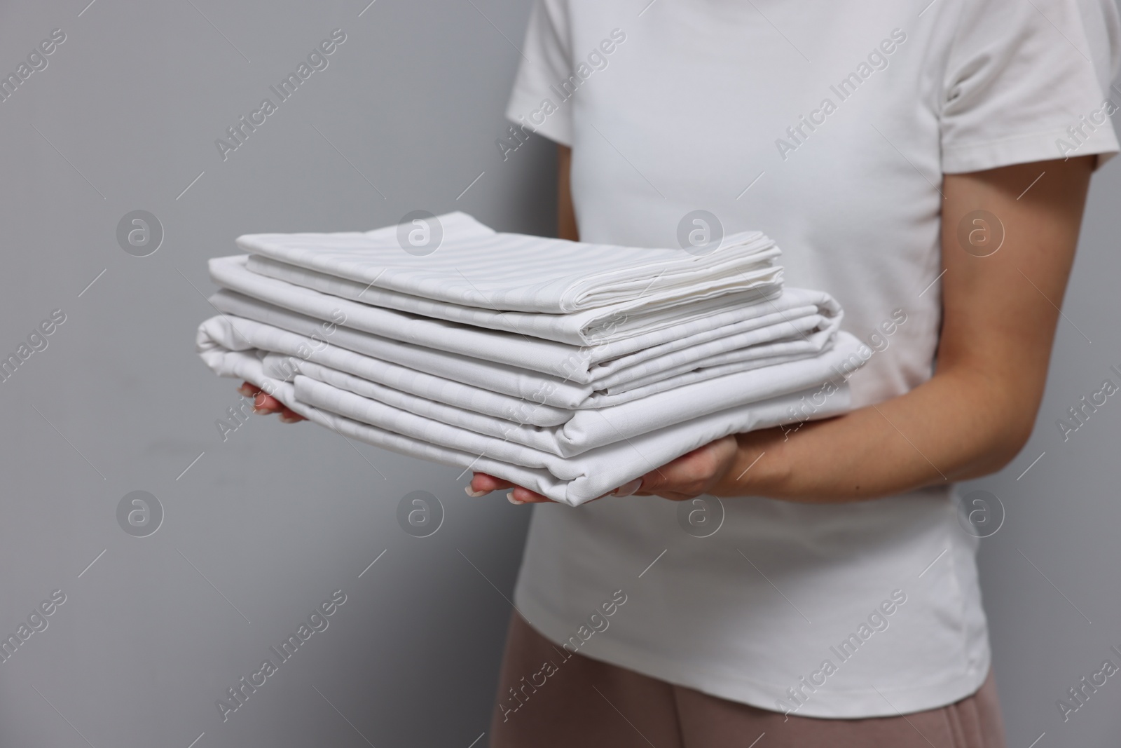 Photo of Woman with clean bed linens on grey background, closeup