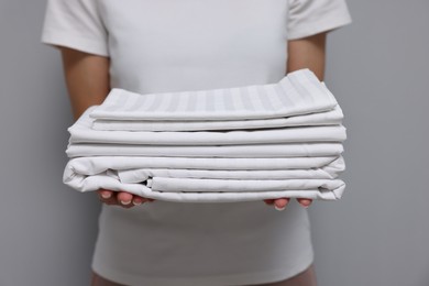 Woman with clean bed linens on grey background, closeup