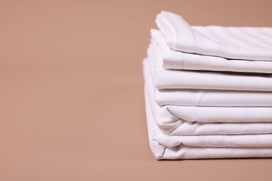 Photo of Stack of clean bed linens on beige background, closeup. Space for text