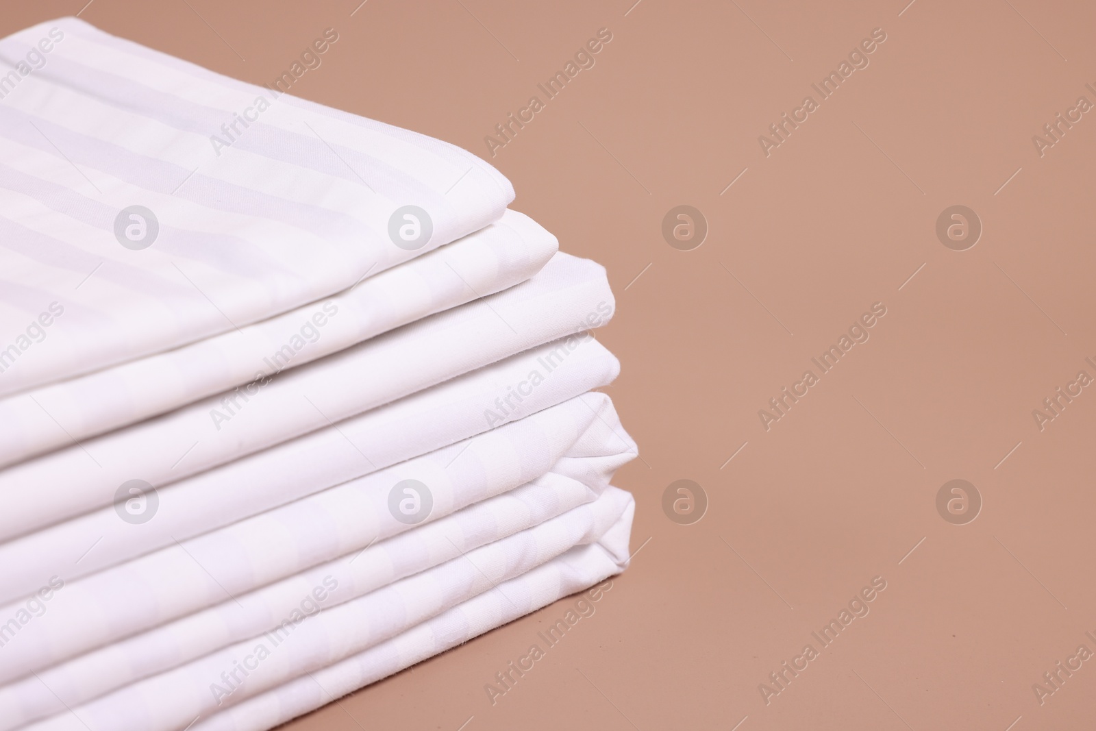 Photo of Stack of clean bed linens on beige background, closeup. Space for text