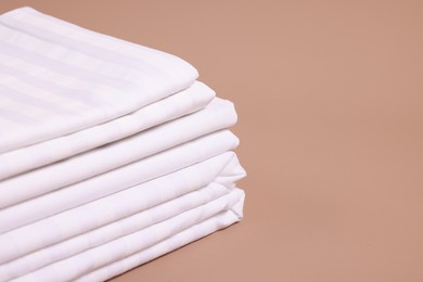 Photo of Stack of clean bed linens on beige background, closeup. Space for text