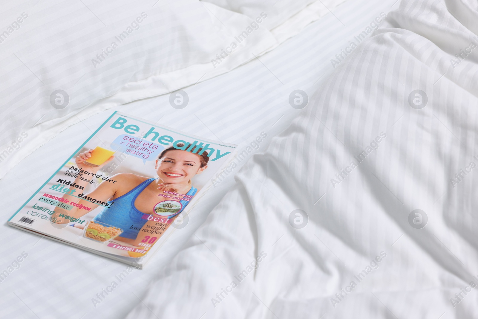 Photo of One magazine on bed with clean linens indoors