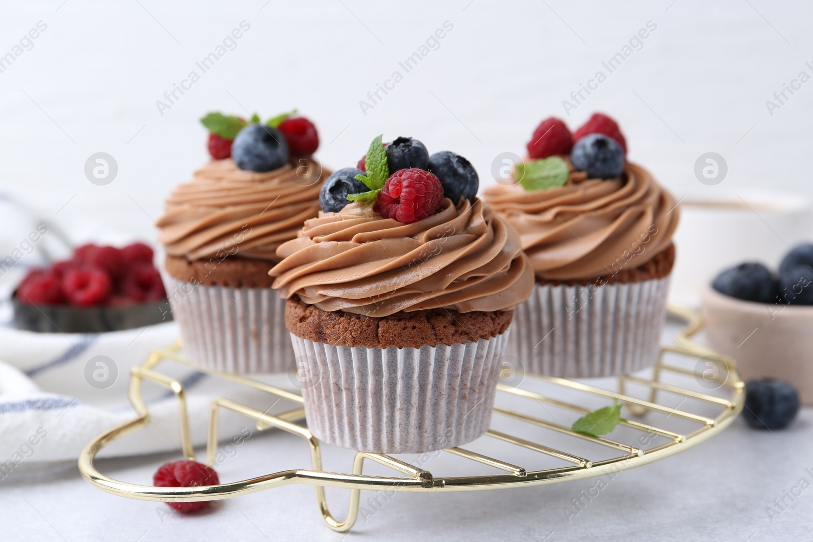 Photo of Tasty cupcakes with chocolate cream and berries on white table, closeup