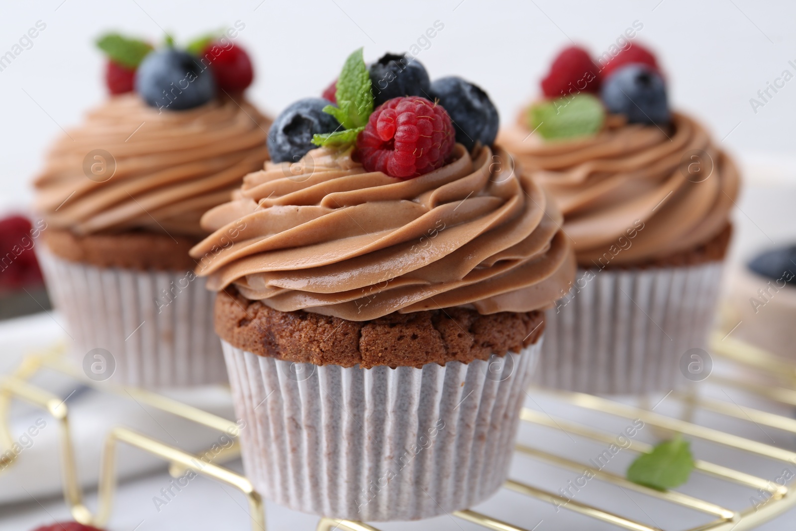 Photo of Tasty cupcakes with chocolate cream and berries on white table, closeup