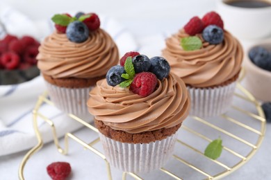 Photo of Tasty cupcakes with chocolate cream and berries on white table, closeup